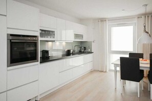 A modern kitchen with white cabinetry, a built-in oven, and a dining area with a table and chairs. - Holiday apartment with 1 bedroom (Scharbeutz)