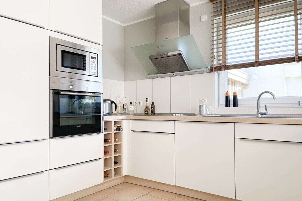 Ett modernt kök med inbyggda vitvaror, ett fönster med persienner och en stilren, minimalistisk design.