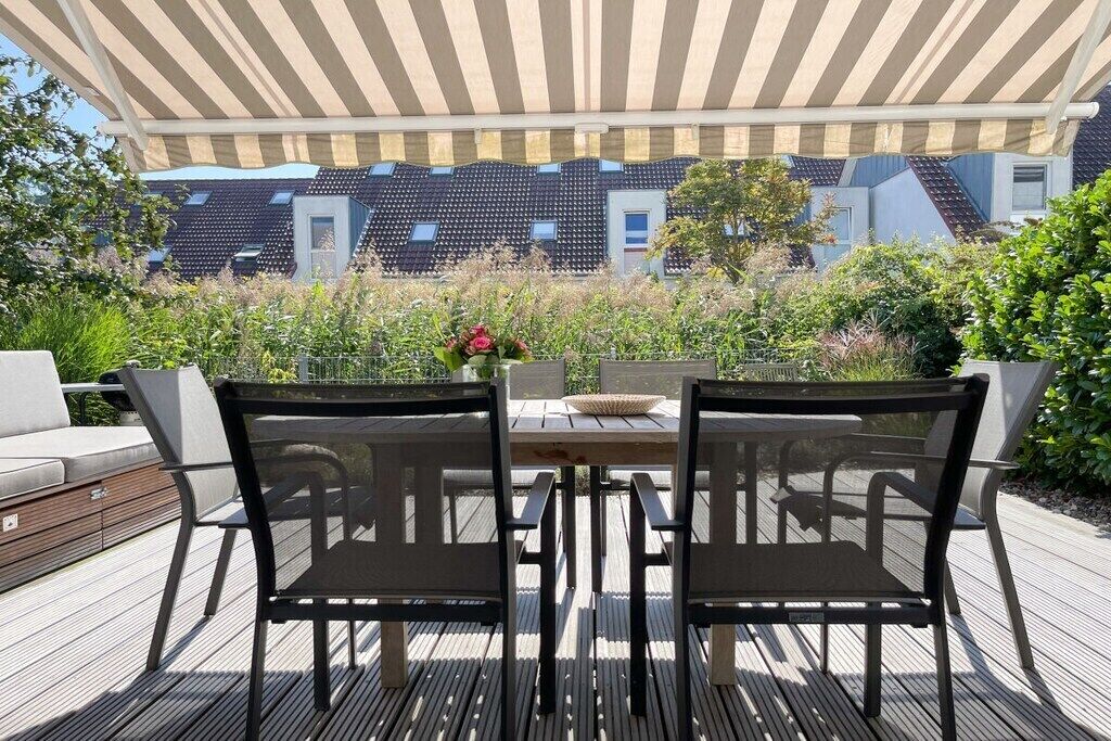 Un patio al aire libre con una mesa y sillas, rodeado de follaje y vistas a edificios.