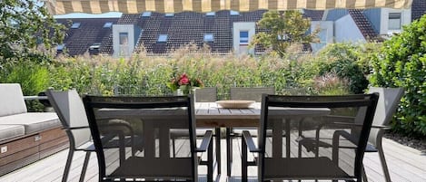 An outdoor patio with a table and chairs, surrounded by greenery and a view of buildings.