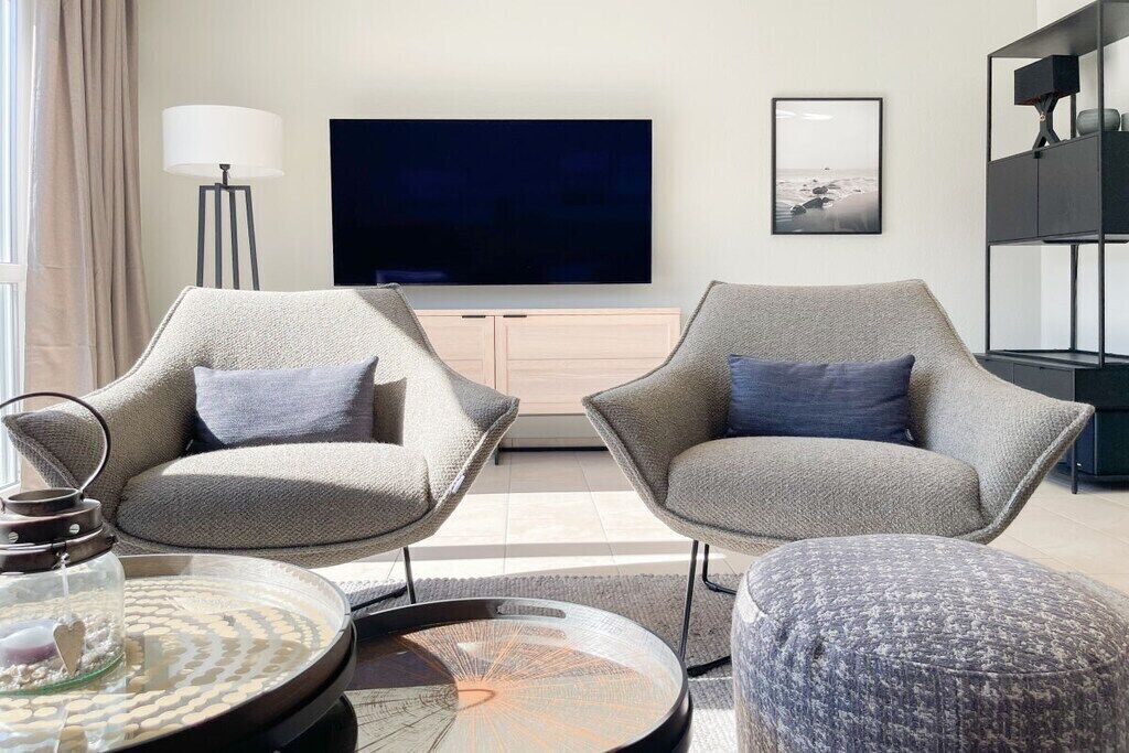 Un salon moderne avec deux fauteuils, une table basse, un téléviseur et une bibliothèque.