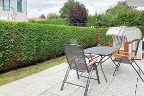 An outdoor patio with a table and chairs, a hedge, and a building in the background. - Holiday apartment with 1 bedroom (Timmendorfer Strand)