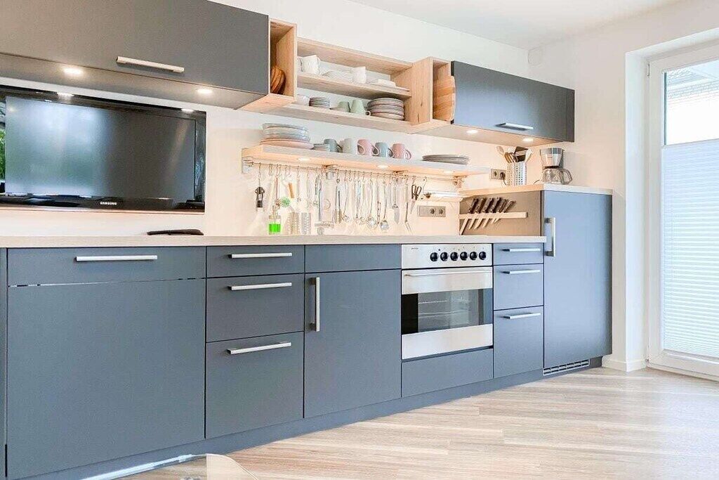 Een moderne keuken met grijze kastjes, een inbouwoven en een televisie.