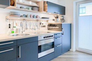 A modern kitchen with a built-in oven, a sink, and a variety of utensils hanging above the counter. - Holiday apartment with 1 bedroom (Timmendorfer Strand)