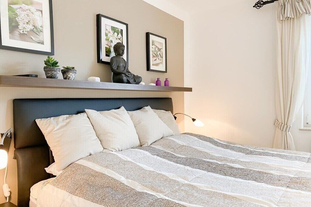 A neatly made bed with a striped bedspread, a headboard, and a wall-mounted shelf with decorative items.