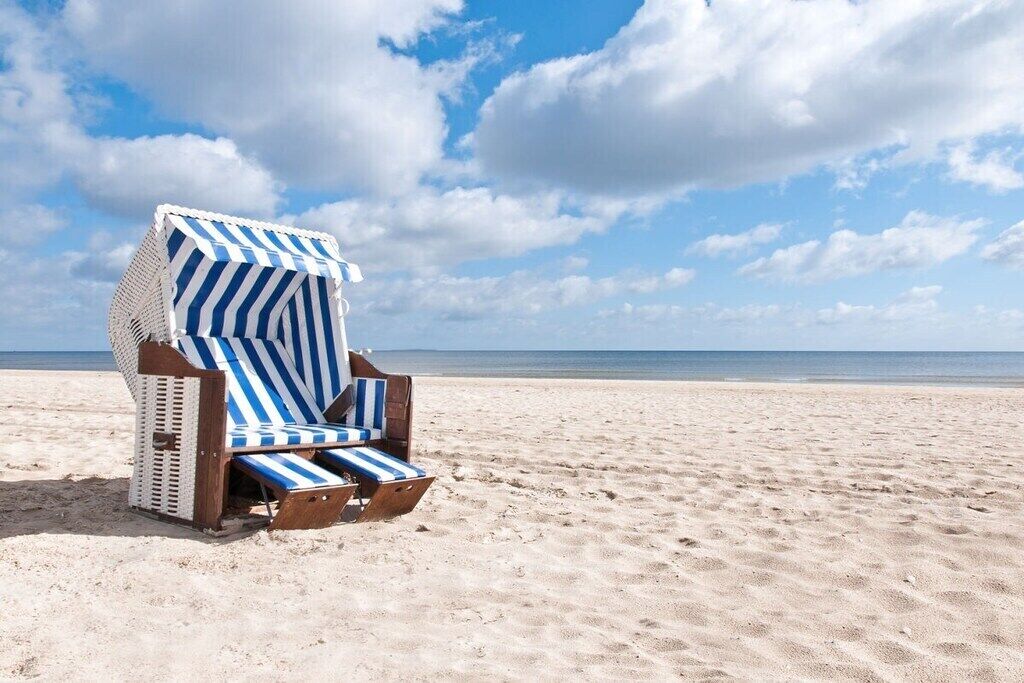 A beach chair with a striped cover on a sandy beach.