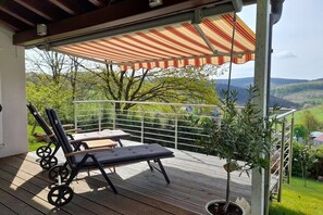 A covered outdoor seating area with a view of a hilly landscape. - Holiday home in Bürberg with swimming pool (Bürberg)