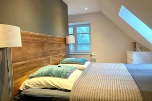 A bedroom with a sloped ceiling, a bed with a quilted cover, a bedside lamp, and a window with a view of trees. - I have a house by the lake, apartment 3 (Hohen Viecheln)