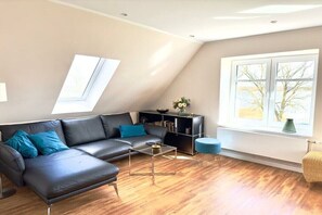Un salon moderne avec un canapé d’angle, une table basse en verre et une grande fenêtre offrant une belle vue.