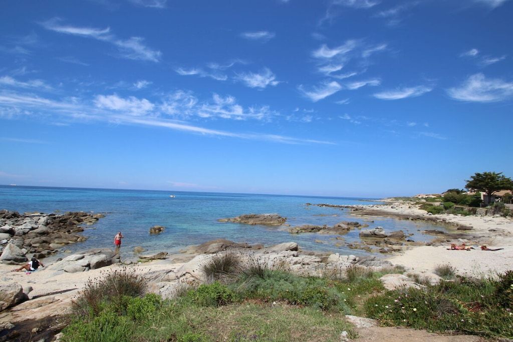 A rocky beach with clear blue water and a few people.