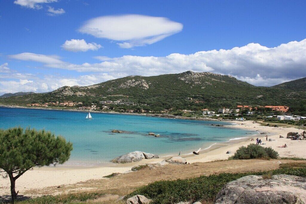 A coastal landscape with a beach, clear blue water, and a sailboat.