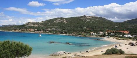 A coastal landscape with a beach, clear blue water, and a sailboat.