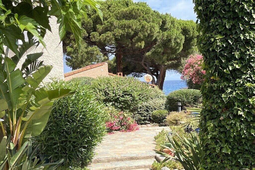 A garden pathway leading to a building with a view of the sea.