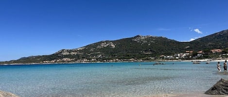 En strand med klart vatten, en sandstrand och ett berg i bakgrunden.