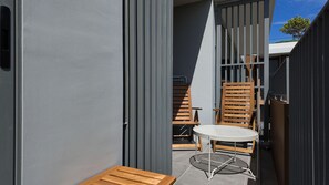 A modern outdoor seating area with a round table and two wooden chairs, enclosed by a metal fence and a grey wall. - 2BR family suite near Boat Lagoon (BangTao)