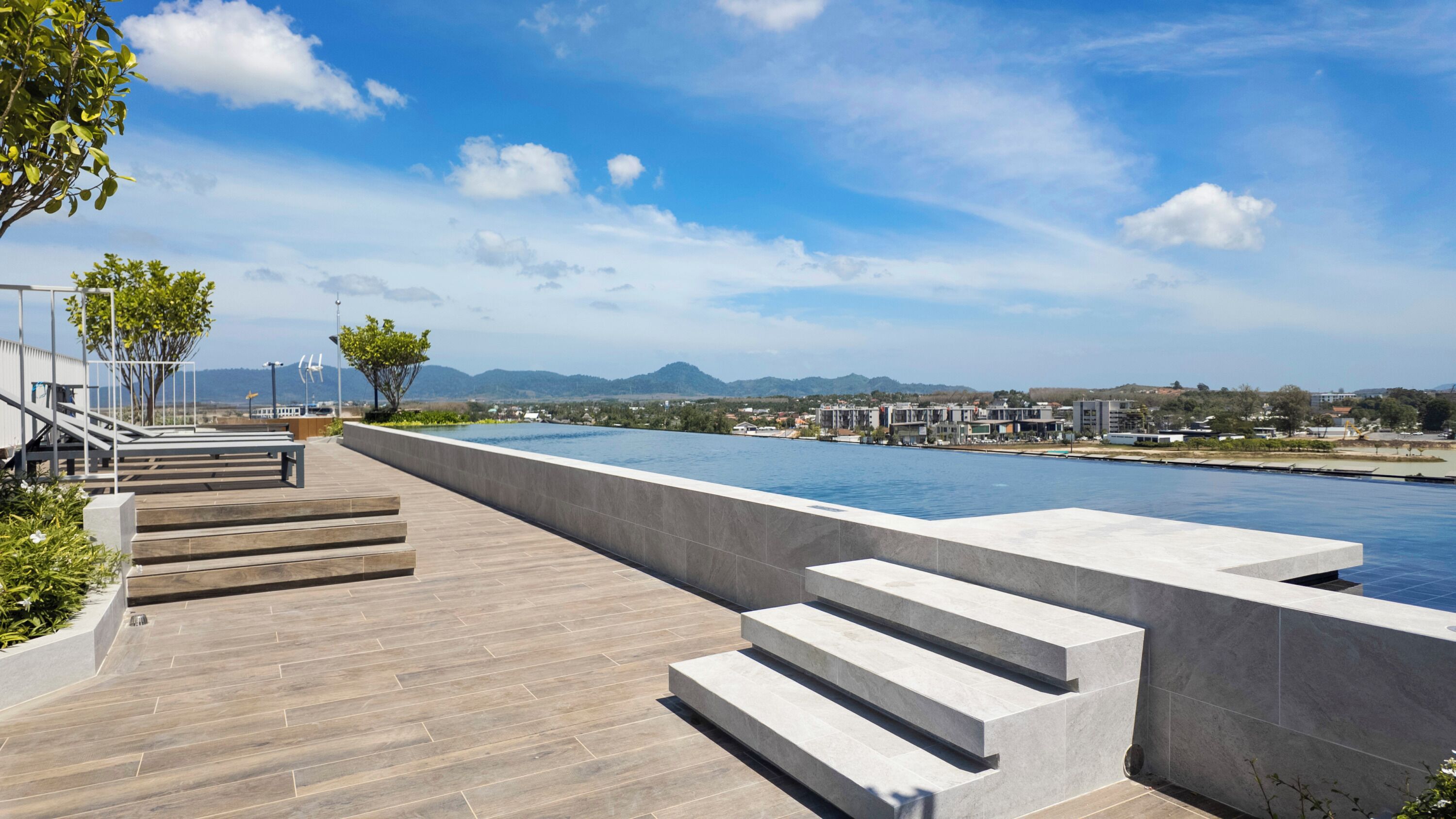 A modern outdoor swimming pool area with steps leading down to the water, surrounded by a clear sky and distant mountains.