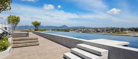 A modern outdoor swimming pool area with steps leading down to the water, surrounded by a clear sky and distant mountains.