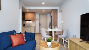 A modern living room with a blue sofa, a wooden coffee table, and a TV on a wooden stand. - 2BR family suite near Boat Lagoon (BangTao)