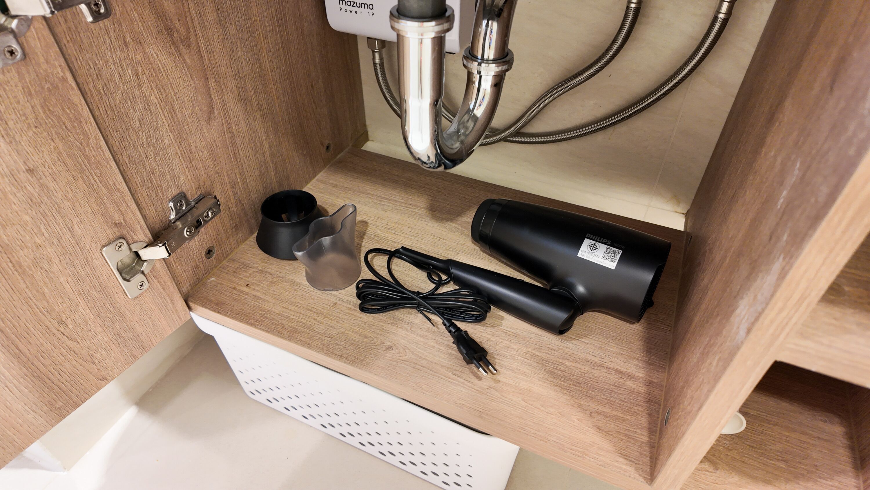 A wooden cabinet with a white drawer, containing a black cylindrical object, a black cylindrical object with a label, and a black cable.