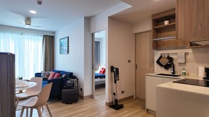 A modern apartment with a dining area, a living room with a sofa, a kitchen with a sink and stove, and a hallway leading to another room. - 2BR family suite near Boat Lagoon (BangTao)