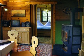 Interior acollidor d'una cabana amb un llit, una llar de foc, parets de fusta i una televisió.