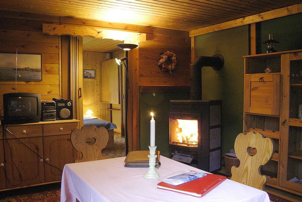 A cozy cabin interior with a wooden interior, a fireplace, a table with a book and a candle, and a television set.