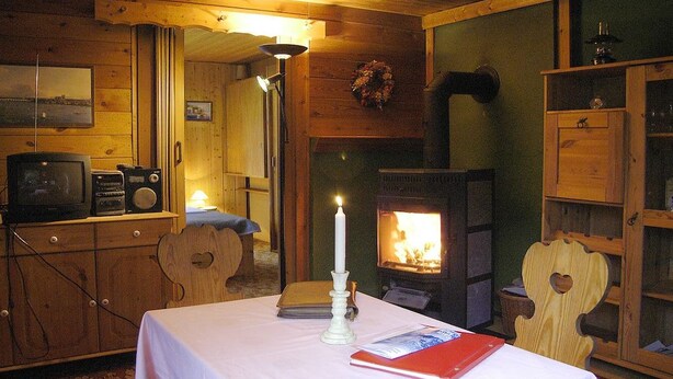 A cozy cabin interior with a wooden interior, a fireplace, a table with a book and a candle, and a television set. - Holiday home with 1 bedroom (Kurort Oybin)