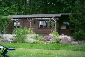 A rustic cabin with a porch, surrounded by a well-maintained garden with various plants and flowers. - Holiday home with 1 bedroom (Kurort Oybin)