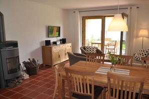 A dining area with a wooden table and chairs, a fireplace, and a view through a glass door. - Lilac House on the Rüsterhof (Rietz-Neuendorf)