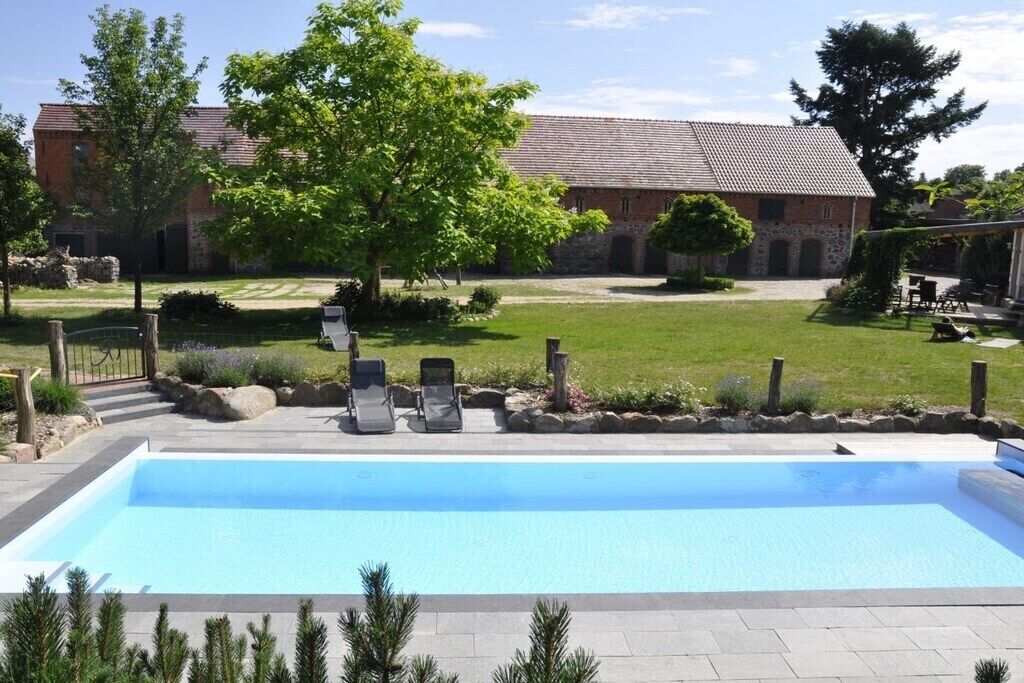 A swimming pool with lounge chairs, a stone building with a tiled roof, and a grassy courtyard.