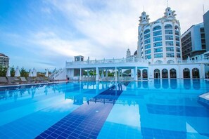 Una amplia piscina con un edificio blanco que tiene ventanas arqueadas y un balcón al fondo.