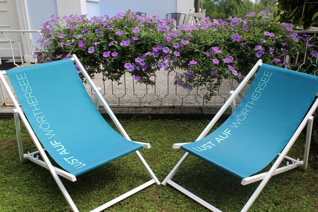 Two lounge chairs with 'LUST AUF WÖRTHSEE' text, positioned in front of a flower bed with purple flowers.