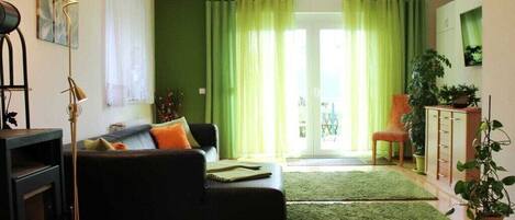 Una sala de estar con un sofá, una lámpara de pie, un televisor y una alfombra verde.