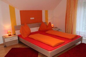 A bedroom with a wooden bed, red bedding, and orange pillows. - Villa Waldbach on Lake Wörthersee (Krumpendorf)