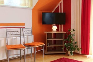 A room with a bed, a television, a lamp, a plant, and a red rug. - Villa Waldbach on Lake Wörthersee (Krumpendorf)