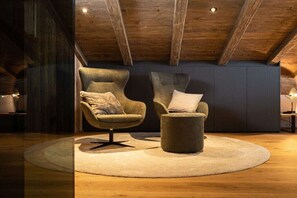 A cozy seating area with two armchairs and a ottoman, a wooden ceiling, and a dark wall.