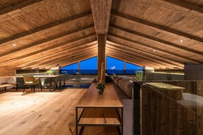 Ein Innenraum mit hoher Decke, Holzbalken, einer Essecke und Blick zum Himmel.