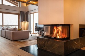 Ein modernes Wohnzimmer mit Kamin, einer Couch, einem Fernseher und einem großen Fenster.