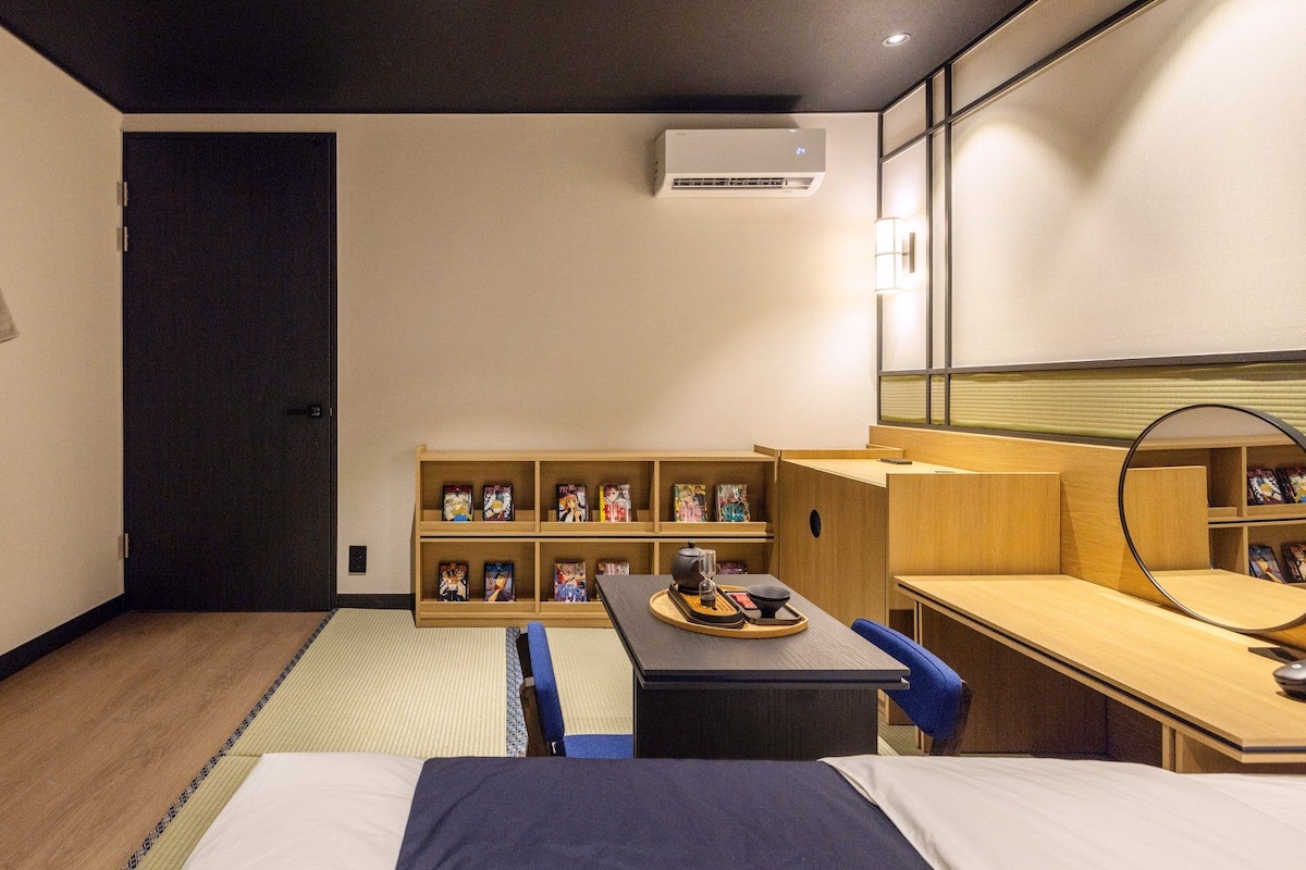 Habitación de hotel con cama, escritorio, silla, estantería llena de libros y una bata colgada en la pared.