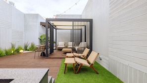 Un patio con mobiliario exterior, una pérgola y un pequeño césped.