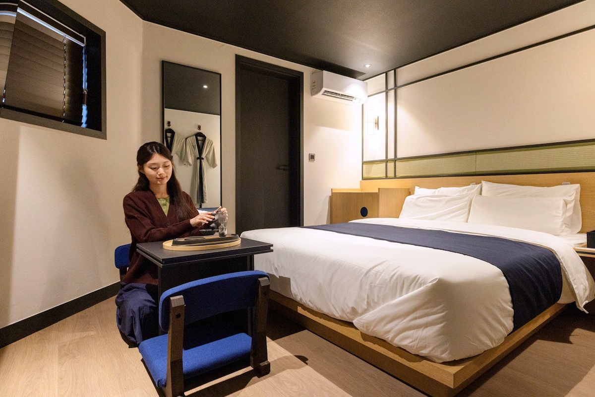 Habitación de hotel con cama, escritorio, silla y ventana con persianas.