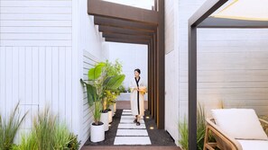 Un sendero que conduce a una habitación con vistas a un jardín, un banco de madera y una persona vestida con traje tradicional.