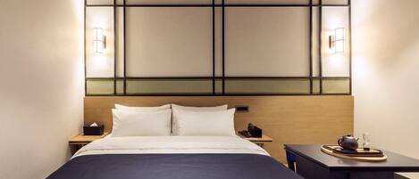 A hotel room with a bed, bedside tables, a desk with a chair, and wall-mounted lighting.