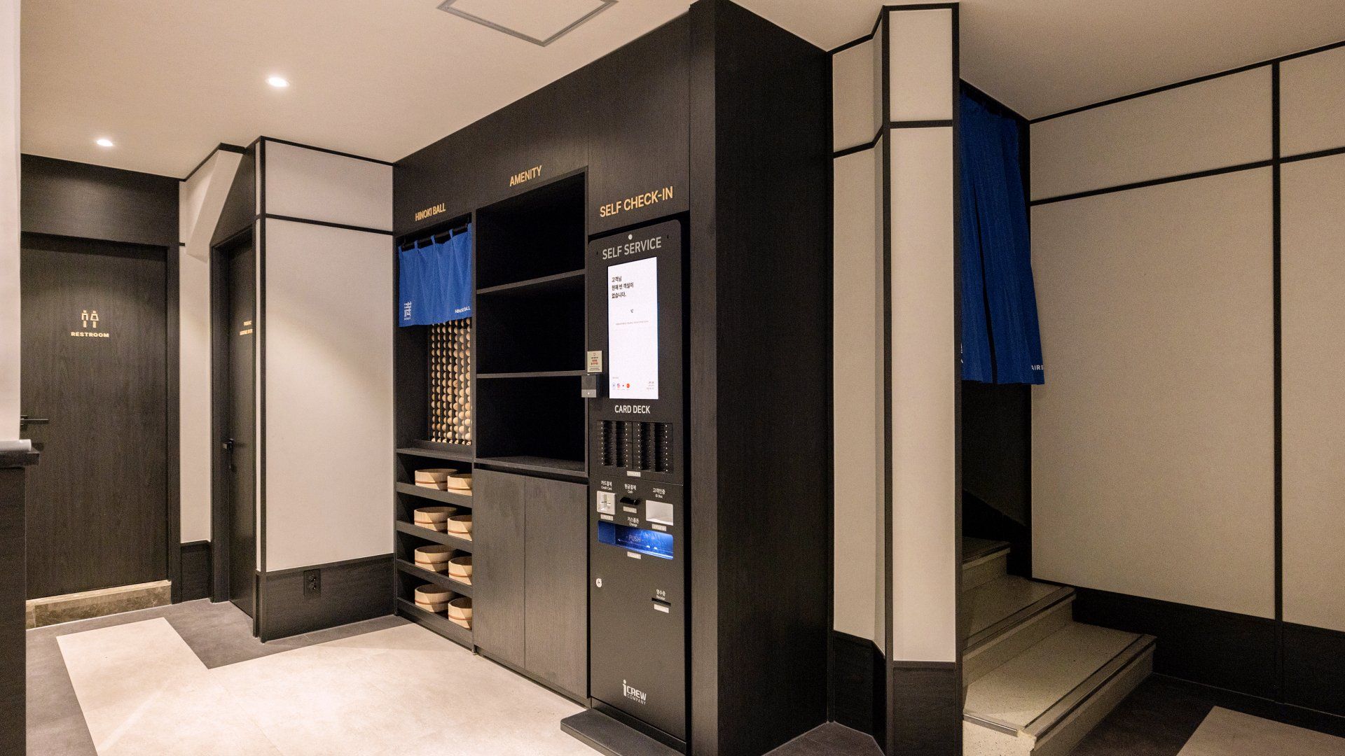 A hotel room with a self-service check-in kiosk, a minibar, and a view of the hallway.