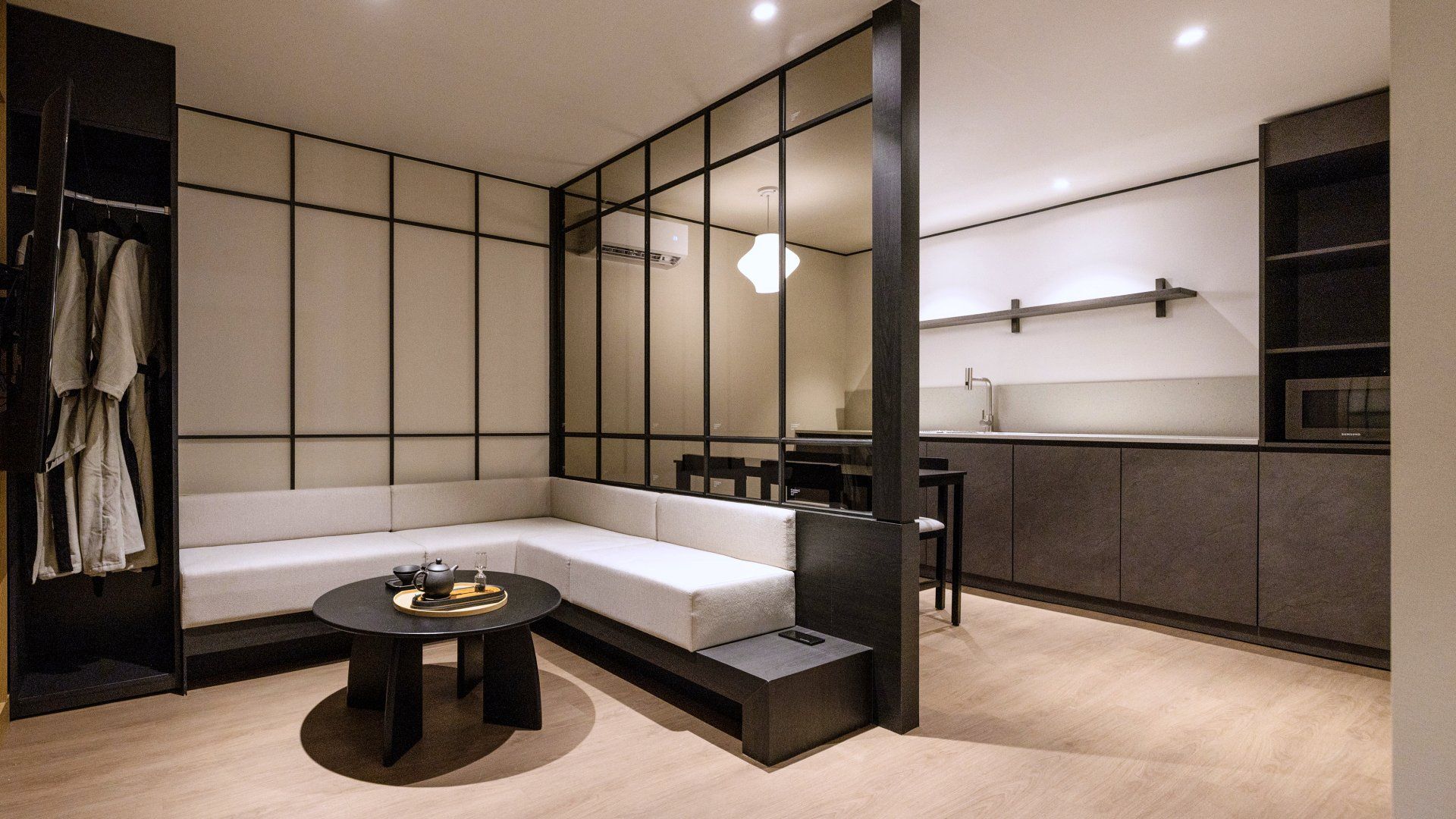 Un intérieur moderne comprenant un canapé d’angle, une table basse ronde, un coin repas et une petite cuisine.
