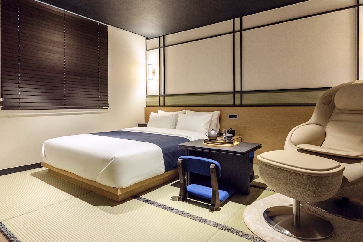 Una habitación de hotel con cama, una silla, una mesita y una lámpara en la pared.