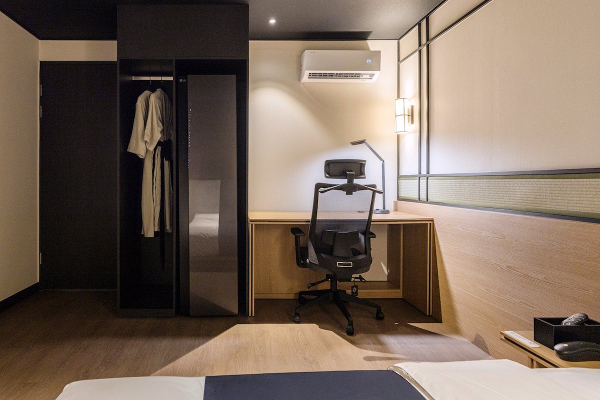 Una habitación de hotel con cama, escritorio, silla, aire acondicionado y armario.