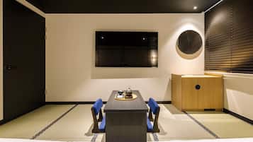 A traditional Japanese-style room with tatami flooring, a low table with a tea set, and a television mounted on the wall.