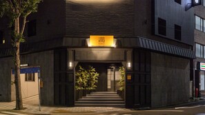 Een gebouw met een bord waarop 'MITSUYA RYOKAN & HOTEL' staat, een trap die omhoog leidt en een parkeersignaal aan de linkerkant.