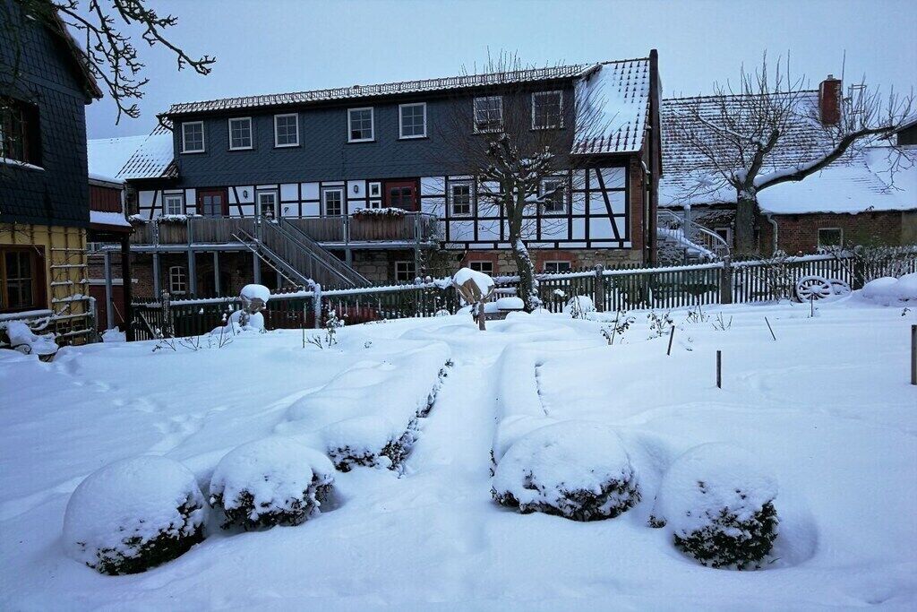A snow-covered courtyard with a traditional building featuring a gabled roof and a staircase leading to a door.